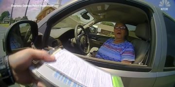 Police officer handing ticket to driver through window.