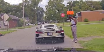 Man standing by sports car near stop sign.