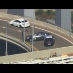 Police cars block dark vehicle on highway ramp.