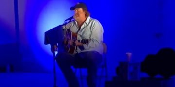 Musician performing acoustic guitar in blue lighting.