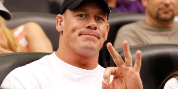 Person in cap making hand gesture at event.