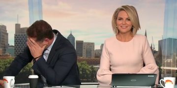 News anchors on set, one laughing, one embarrassed.