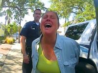 Police officer arrests woman outdoors, sunny day.