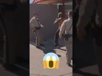 Police officers confront a man outdoors.
