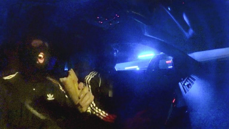 Masked person eating sandwich in dark car, blue light.