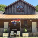 Rustic log building with 'Open' flag and chairs.
