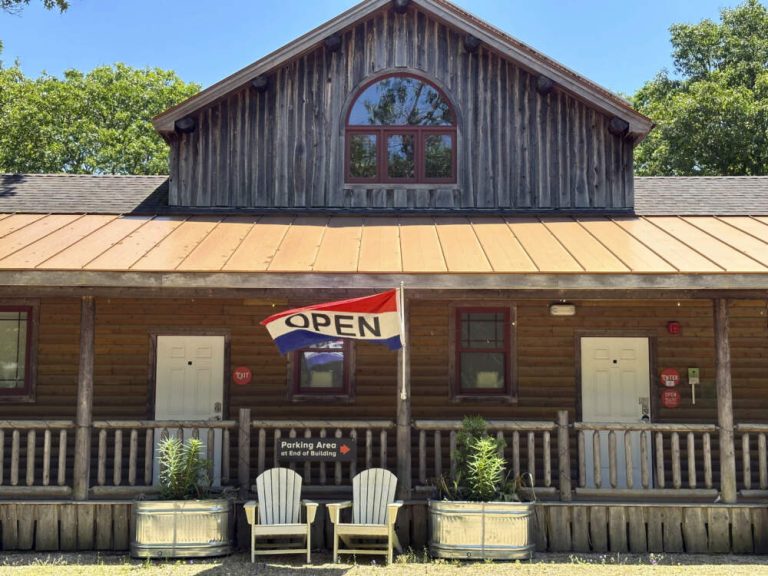 Rustic log building with 'Open' flag and chairs.