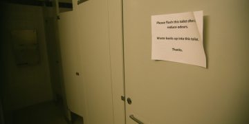 Public restroom stall with sign instructing frequent flushing.