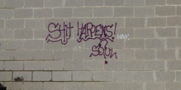 Graffiti on brick wall reading 'S*** Happens!'