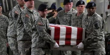 Soldiers carry casket draped in American flag.