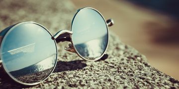 Sunglasses reflecting ocean on sandy beach.