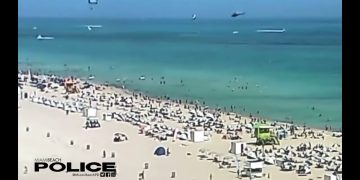 Crowded Miami Beach with parasailers and sunbathers.