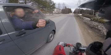 Biker giving fist bump to car passenger on road.