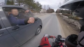 Biker giving fist bump to car passenger on road.