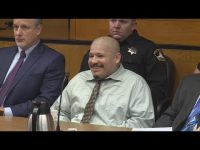 Courtroom scene with seated individuals, one smiling.