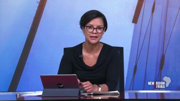 News anchor at desk with laptop and notes.