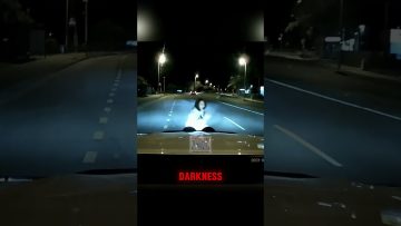Dark road with car headlights and person.