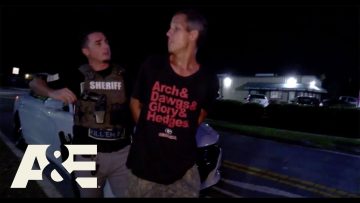 Sheriff detaining man at night near parked cars.