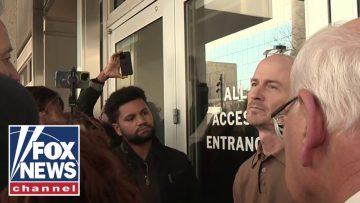 Group outside a building entrance being filmed.