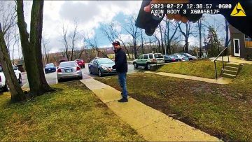 Person walking on sidewalk near parked cars, winter trees.