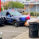 Police cars surround white car in parking lot incident.