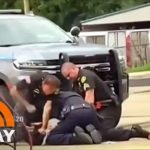 Police restrain person on ground near vehicle.