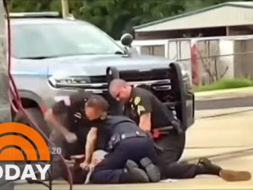 Police restrain person on ground near vehicle.