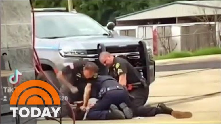 Police restrain person on ground near vehicle.