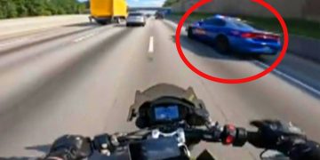 Motorcyclist on highway near a police car.