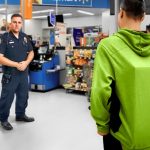 Store employee and officer confront customer in green hoodie.