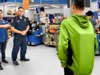 Store employee and officer confront customer in green hoodie.