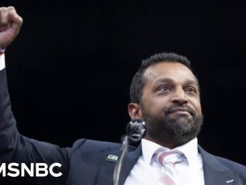 Person raising fist, wearing suit on stage.