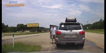 Man exits silver SUV near roadside sign.