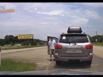 Man exits silver SUV near roadside sign.