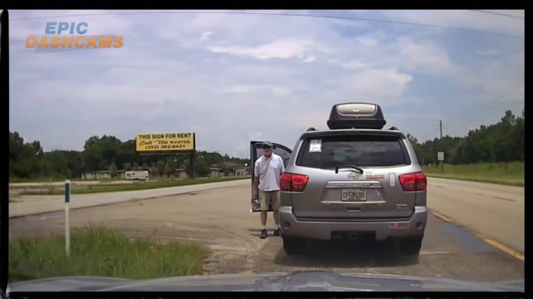 Man exits silver SUV near roadside sign.