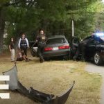 Police at car crash scene with suspect detained.