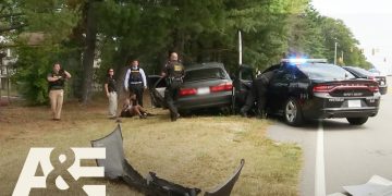 Police at car crash scene with suspect detained.