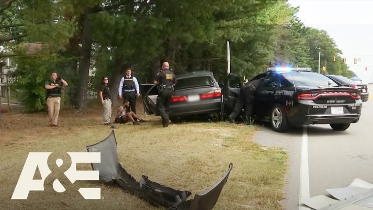 Police at car crash scene with suspect detained.