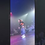 Person dancing onstage with audience behind.