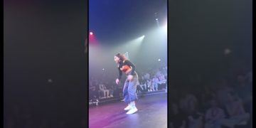 Person dancing onstage with audience behind.
