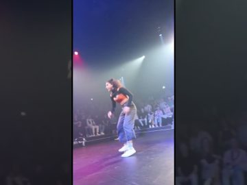 Person dancing onstage with audience behind.