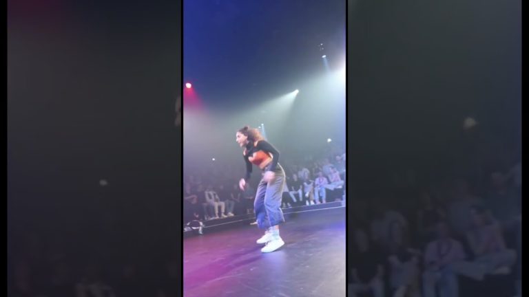 Person dancing onstage with audience behind.