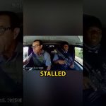 Car interior with driver and armed passenger.
