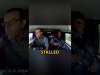 Car interior with driver and armed passenger.