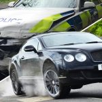 Black car speeds past damaged police vehicle.