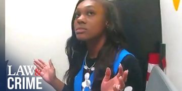 Person in office setting, hands raised, looking up.