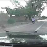 Dashcam captures person walking on road, trees nearby.