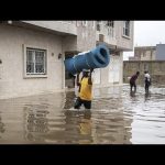 People wading through flooded street carrying items.
