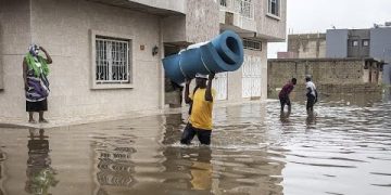 People wading through flooded street carrying items.