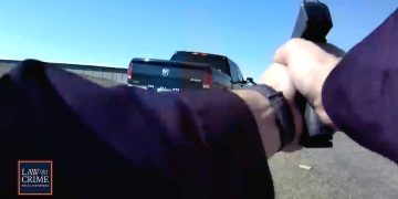 Person aiming gun at truck on road.